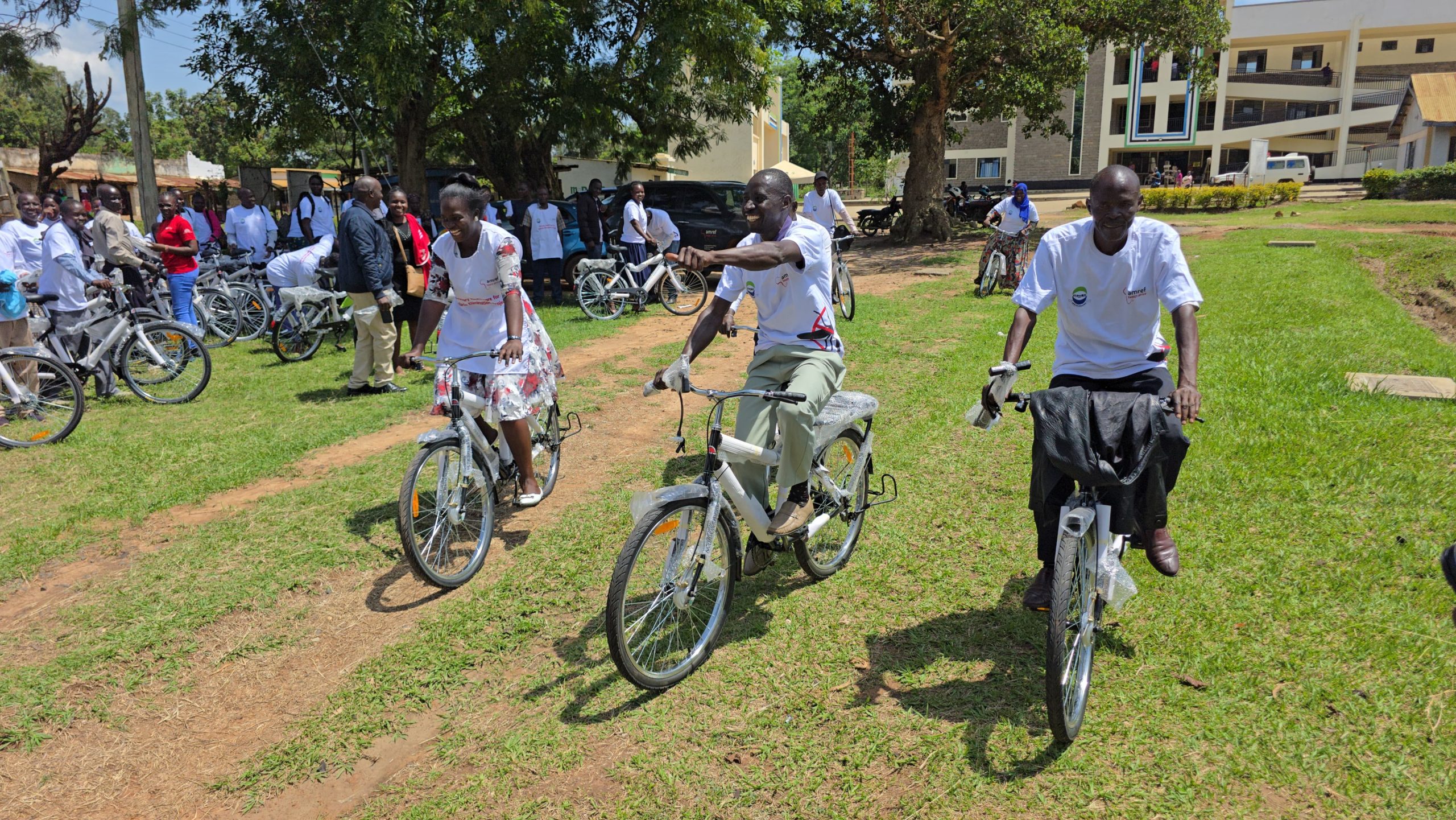 Health workers practice cycling. Three cyclists are in the foreground, and many other people with bikes mill in the background.