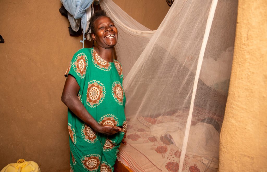 Caroline Atieno stands beside a mosquito net in Siaya County, Kenya. (c) Amref Health Africa/Kennedy Musyoka